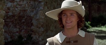 Movie still from “The Three Musketeers” (1993), directed by Stephen Herek – A young man wearing a white hat smiling for the camera; Close Up shot, Over the shoulder angle