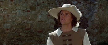 Movie still from “The Three Musketeers” (1993), directed by Stephen Herek – A man wearing a cowboy hat standing in front of a stone wall; Close Up shot, Low angle
