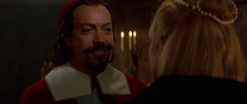 Movie still from “The Three Musketeers” (1993), directed by Stephen Herek – A man with a beard and a mustache is talking to a woman in front of candles; Close Up shot, Over the shoulder angle