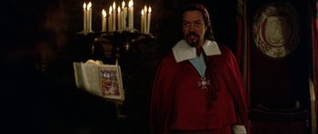 Movie still from “The Three Musketeers” (1993), directed by Stephen Herek – A man in a red robe standing in front of candles; Medium shot, Over the shoulder angle