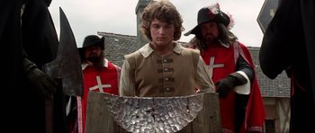 Movie still from “The Three Musketeers” (1993), directed by Stephen Herek – A man standing in front of two other men in medieval garb; Medium shot, Low angle
