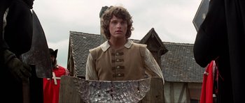 Movie still from “The Three Musketeers” (1993), directed by Stephen Herek – A young man in a brown shirt holding an umbrella; Medium shot, Low angle