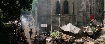 Movie still from “The Three Musketeers” (1993), directed by Stephen Herek – A group of people standing next to a cart filled with produce; Extreme Wide shot, High angle