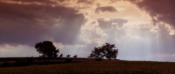 Movie still from “The Three Musketeers” (1993), directed by Stephen Herek – Three people on horseback ride through a field under a cloudy sky; Extreme Wide shot, Low angle
