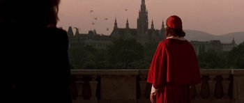 Movie still from “The Three Musketeers” (1993), directed by Stephen Herek – A man in a red robe looking out at a castle; Wide shot, Over the shoulder angle