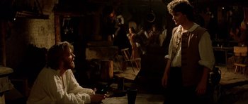 Movie still from “The Three Musketeers” (1993), directed by Stephen Herek – Two people sitting in a room with a man standing next to them; Medium shot, Over the shoulder angle