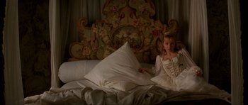 Movie still from “The Three Musketeers” (1993), directed by Stephen Herek – A young girl in a white dress sitting on a bed with pillows; Medium shot, High angle