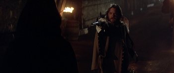 Movie still from “The Three Musketeers” (1993), directed by Stephen Herek – A man holding a gun in a dark room; Medium shot, Over the shoulder angle