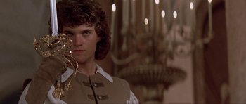 Movie still from “The Three Musketeers” (1993), directed by Stephen Herek – A man with long brown hair holding a gold chain; Close Up shot, Low angle