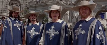 Movie still from “The Three Musketeers” (1993), directed by Stephen Herek – A group of men in medieval garb standing next to each other; Medium shot, Low angle