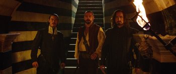 Movie still from “The Three Musketeers” (2011), directed by Paul W.S. Anderson – A group of men standing next to each other in front of a staircase; Medium shot, Low angle