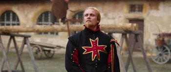 Movie still from “The Three Musketeers” (2011), directed by Paul W.S. Anderson – A man wearing a black and red outfit with a cross on it; Medium shot, Over the shoulder angle