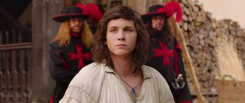 Movie still from “The Three Musketeers” (2011), directed by Paul W.S. Anderson – A young man in medieval garb stands in front of a group of men in medieval garb; Close Up shot, Over the shoulder angle