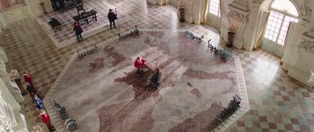 Movie still from “The Three Musketeers” (2011), directed by Paul W.S. Anderson – Two people are sitting on the floor of a large room; Extreme Wide shot, High angle