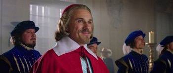 Movie still from “The Three Musketeers” (2011), directed by Paul W.S. Anderson – A man with long blonde hair wearing a red outfit; Close Up shot, Over the shoulder angle