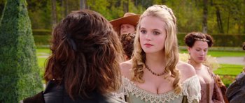 Movie still from “The Three Musketeers” (2011), directed by Paul W.S. Anderson – A young woman with long blonde curly hair wearing a necklace; Close Up shot, Over the shoulder angle