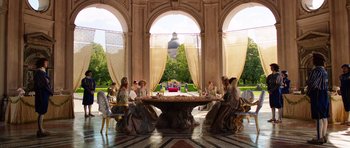 Movie still from “The Three Musketeers” (2011), directed by Paul W.S. Anderson – A group of people sitting at a table in front of an arch window; Wide shot, High angle