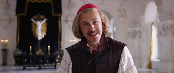Movie still from “The Three Musketeers” (2011), directed by Paul W.S. Anderson – A man with long blonde hair wearing a red hat; Medium shot, Over the shoulder angle
