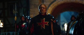 Movie still from “The Three Musketeers” (2011), directed by Paul W.S. Anderson – A man in a black and red jacket standing in front of a group of people; Medium shot, Over the shoulder angle