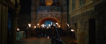 Movie still from “The Three Musketeers” (2011), directed by Paul W.S. Anderson – A group of people are standing in front of a building with torches; Wide shot, Over the shoulder angle