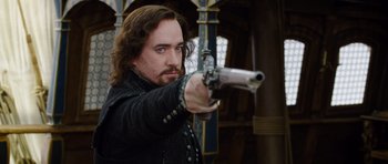 Movie still from “The Three Musketeers” (2011), directed by Paul W.S. Anderson – A man with long hair is holding a gun; Medium shot, Over the shoulder angle