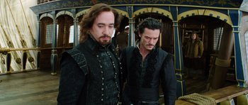 Movie still from “The Three Musketeers” (2011), directed by Paul W.S. Anderson – Two men dressed in medieval garb standing next to each other; Medium shot, Over the shoulder angle