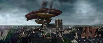 Movie still from “The Three Musketeers” (2011), directed by Paul W.S. Anderson – An airship flying over a city with smoke billowing out of it; Extreme Wide shot, Low angle