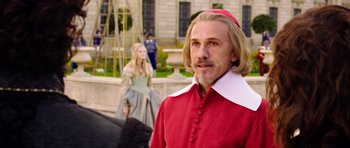 Movie still from “The Three Musketeers” (2011), directed by Paul W.S. Anderson – A man in a red and white outfit standing in front of a woman; Close Up shot, Over the shoulder angle