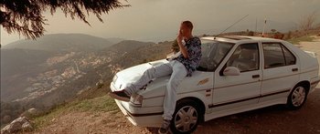 Movie still from “The Transporter” (2002), directed by Corey Yuen – A man sitting on the hood of a car on a hill; Wide shot, Low angle