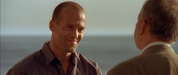 Movie still from “The Transporter” (2002), directed by Corey Yuen – A bald man smiling at the camera while standing next to a woman; Close Up shot, Over the shoulder angle