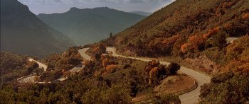 Movie still from “The Transporter” (2002), directed by Corey Yuen – A road going down a hill with trees on the side of it; Extreme Wide shot, High angle