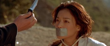 Movie still from “The Transporter” (2002), directed by Corey Yuen – A woman with duct tape around her mouth and holding a pair of shears; Close Up shot, Low angle