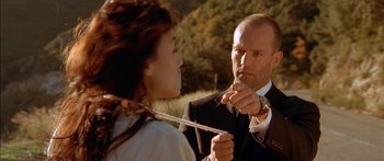 Movie still from “The Transporter” (2002), directed by Corey Yuen – A man in a suit and tie holding a knife to a woman's mouth; Close Up shot, Over the shoulder angle