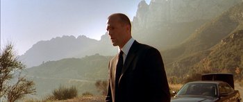 Movie still from “The Transporter” (2002), directed by Corey Yuen – A man in a suit and tie standing in front of mountains; Medium shot, Low angle