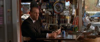 Movie still from “The Transporter” (2002), directed by Corey Yuen – A man sitting at a table in a store holding a cell phone; Medium shot, Low angle