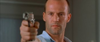 Movie still from “The Transporter” (2002), directed by Corey Yuen – A man holding a gun in his right hand while wearing a blue shirt; Close Up shot, Low angle