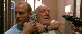 Movie still from “The Transporter” (2002), directed by Corey Yuen – A man with a gun and another man with a watch; Close Up shot, Low angle
