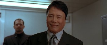 Movie still from “The Transporter” (2002), directed by Corey Yuen – A man wearing a suit and tie smiling for the camera; Close Up shot, Low angle