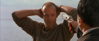 Movie still from “The Transporter” (2002), directed by Corey Yuen – A man holding a gun up to his head in front of a body of water; Close Up shot, Low angle
