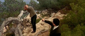 Movie still from “The Transporter” (2002), directed by Corey Yuen – Two men on a rocky hill with a gun pointed at them; Wide shot, Over the shoulder angle