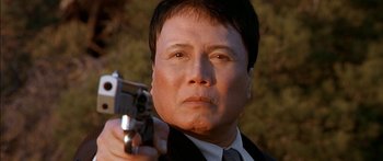 Movie still from “The Transporter” (2002), directed by Corey Yuen – A man in a suit and tie holding a gun in his hand; Close Up shot, Low angle