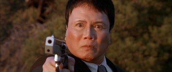 Movie still from “The Transporter” (2002), directed by Corey Yuen – A man in a suit and tie holding a gun in his hand; Close Up shot, Low angle