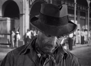 Movie still from “The Treasure of the Sierra Madre” (1948), directed by John Huston – A man wearing a hat standing on the street; Close Up shot, Low angle