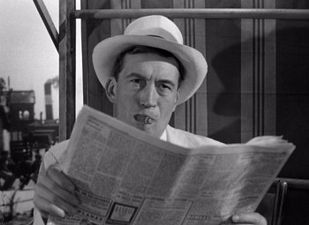 Movie still from “The Treasure of the Sierra Madre” (1948), directed by John Huston – A black and white photo of a man in a hat smoking a cigarette and reading a newspaper; Close Up shot, Low angle