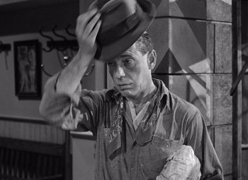 Movie still from “The Treasure of the Sierra Madre” (1948), directed by John Huston – A black and white photo of a man putting on a hat; Medium shot, High angle