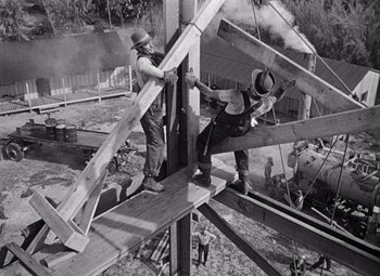 Movie still from “The Treasure of the Sierra Madre” (1948), directed by John Huston – A black and white photo of two men working on a structure; Wide shot, Low angle