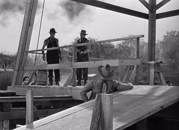 Movie still from “The Treasure of the Sierra Madre” (1948), directed by John Huston – A black and white photo of two men on a bridge; Wide shot, Over the shoulder angle