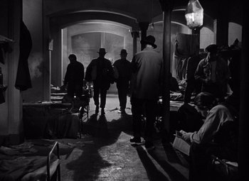Movie still from “The Treasure of the Sierra Madre” (1948), directed by John Huston – A black and white photo of a group of men standing in a room; Wide shot, Low angle