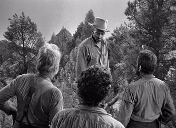 Movie still from “The Treasure of the Sierra Madre” (1948), directed by John Huston – A man in a top hat talking to a group of people; Medium shot, Over the shoulder angle