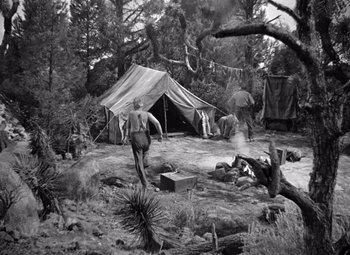Movie still from “The Treasure of the Sierra Madre” (1948), directed by John Huston – An old photo of a man walking in the woods near a tent; Wide shot, High angle